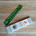 Image de l'encens Ayurvedic sauge blanche en bâtonnets. Cette boite d'encens est posée à côté d'un porte encens en bois coloré en vert foncé sur lequel il y a un bâtonnet d'encens. L'image est prise sur un fond zen. Ces produits sont en vente chez Zen Aatma - boutique zen et ésotérique.