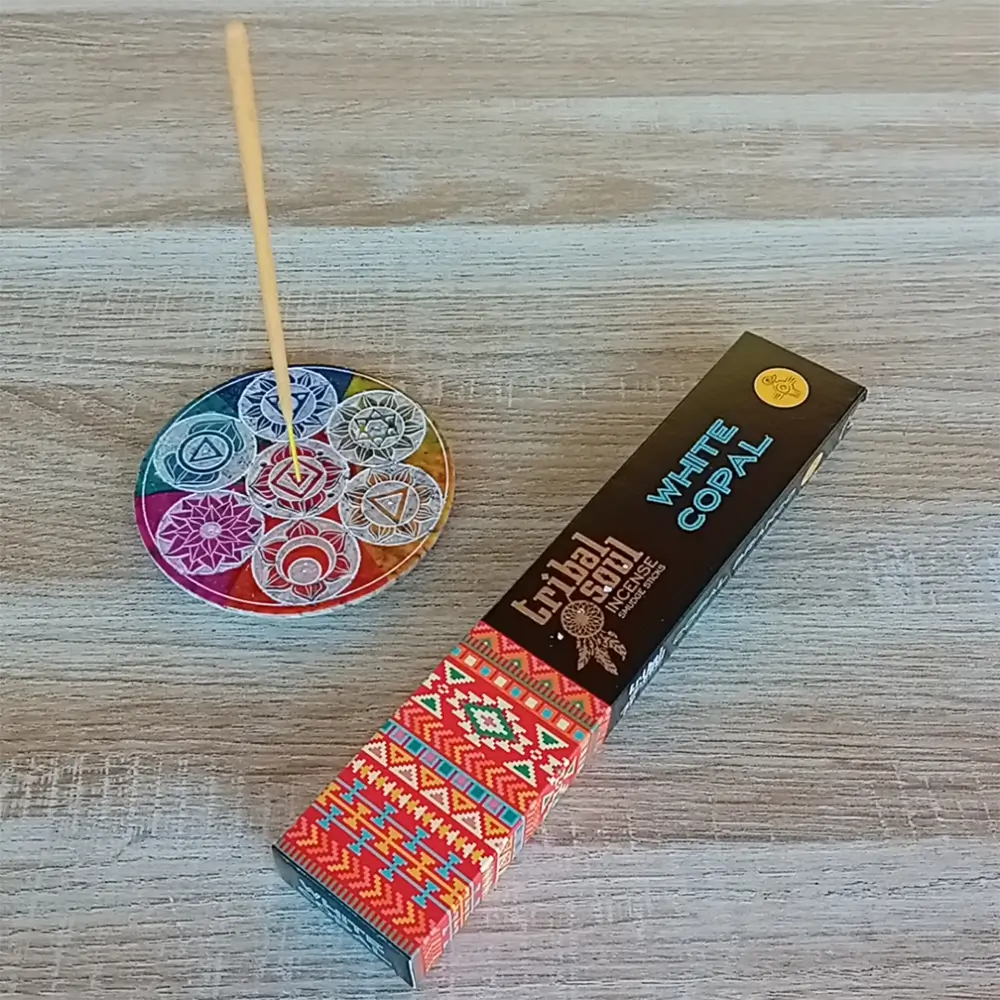 Image de l'encens Tribal Soul Copal blanc en bâtonnets. Cette boite d'encens est posée à côté d'un porte encens rond coloré sur lequel il y a un bâtonnet d'encens au Copal blanc. L'image est prise sur un fond zen. Ces produits sont en vente chez Zen Aatma - boutique zen et ésotérique.
