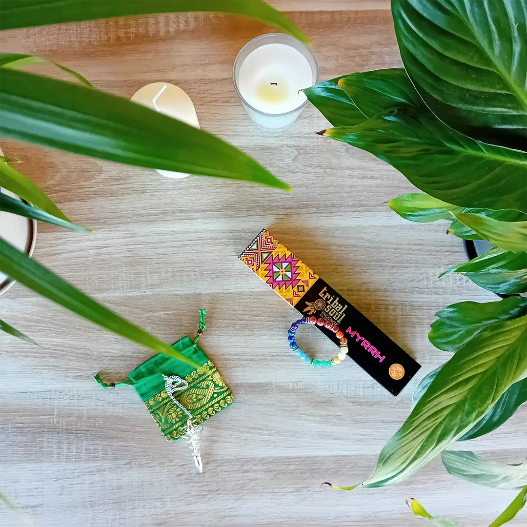 On peut voir une boite d'encens Tribal Soul Myrrh, un bracelet 7 chakras, un pendule spirale argentée grand modèle et une pochette Brocart pour pendule de couleur verte. Ces produits font partie du pack rituels ésotériques de la boutique Zen Aatma. Il y a aussi deux bougies et des plantes vertes. L'ambiance de l'image est très zen. On peut trouver ces produits dans la boutique en ligne d'articles zen et ésotériques Zen Aatma.